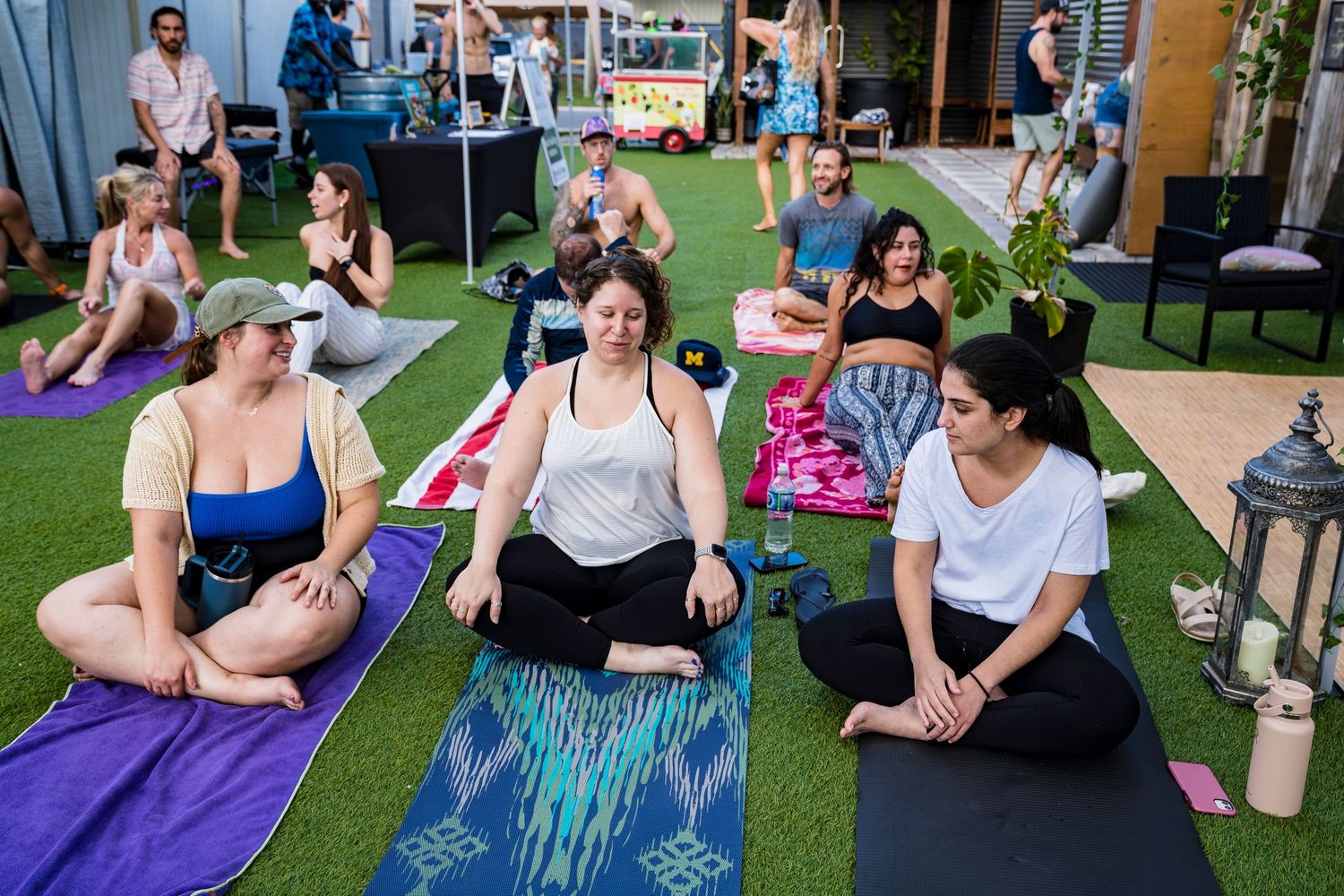 A photo of women sitting on their yoga mats and talking to each other during a yoga event.