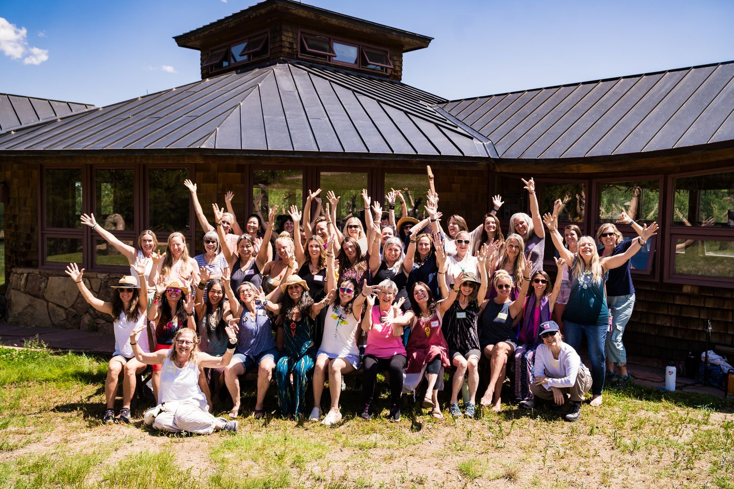 Large group of happy people cheering outside rustic wooden pavilion on sunny day.