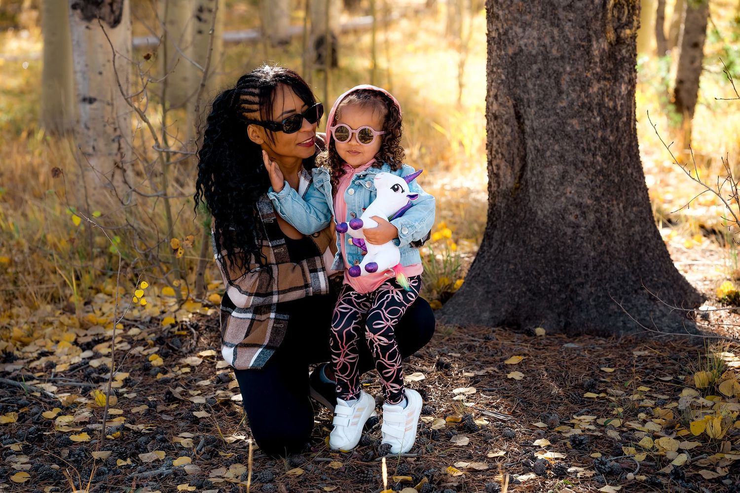 Family enjoying a fall photoshoot in a wooded area with golden autumn leaves scattered on the ground.