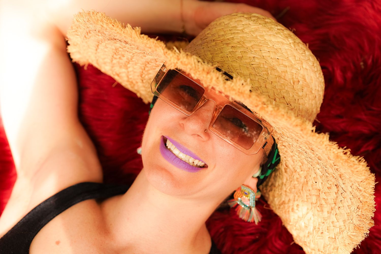 Person wearing a straw hat and sunglasses smiles while relaxing outdoors in bright sunlight.