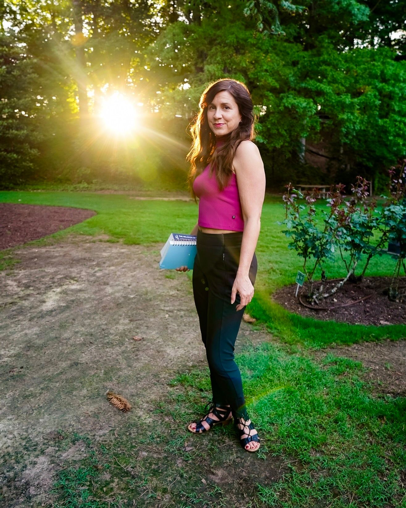 A golden sunset illuminates a garden path with lush greenery and trees creating a magical outdoor atmosphere.