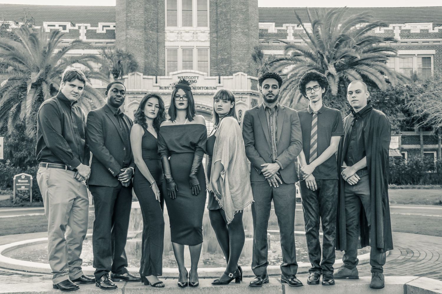 A diverse group of eight professionals posing together outdoors in formal attire near a fountain.