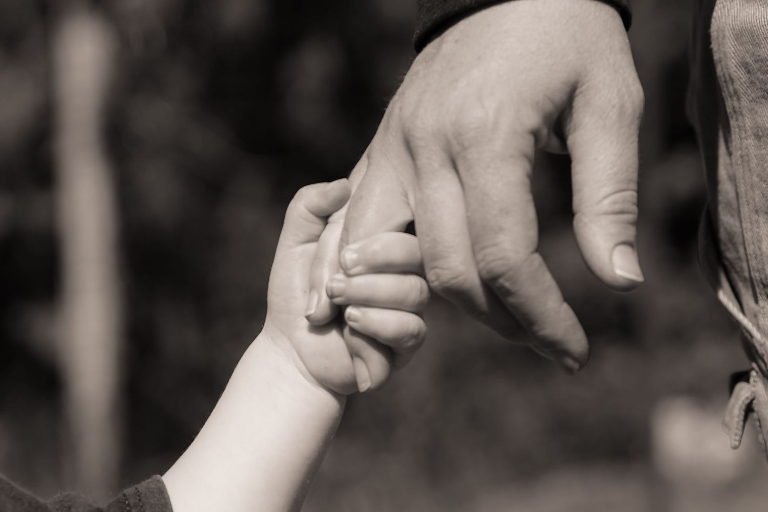 Black and white photo of a child's small hand holding an adult's finger, symbolizing family bond and trust.