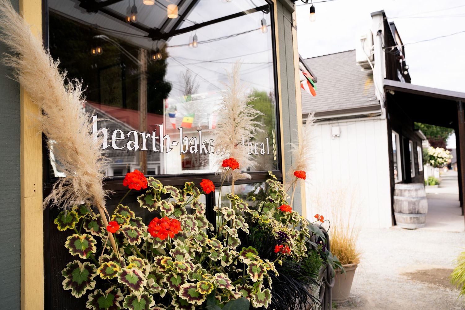 Hearth Bakery storefront with vibrant red geraniums and pampas grass decor outside a charming shop entrance.