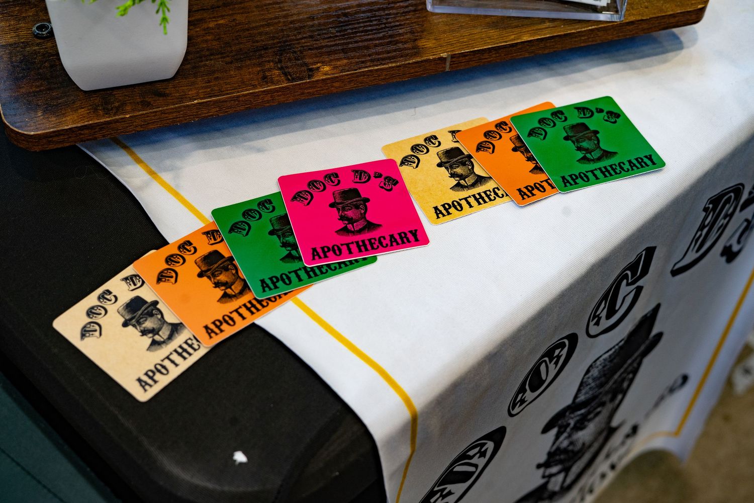 Colorful Apothecary branded stickers in green, orange, pink, and tan displayed on a white tablecloth at a market.