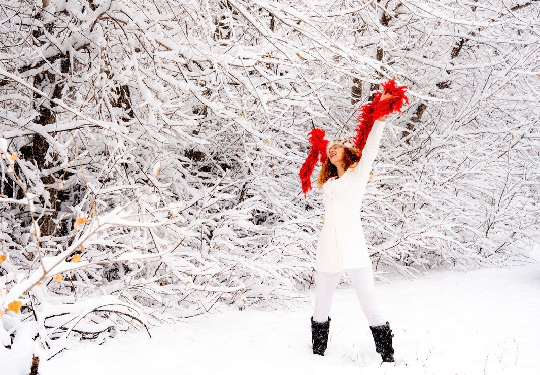 A snowman with red scarf and hat stands in a snowy winter wonderland surrounded by snow-covered trees and branches.