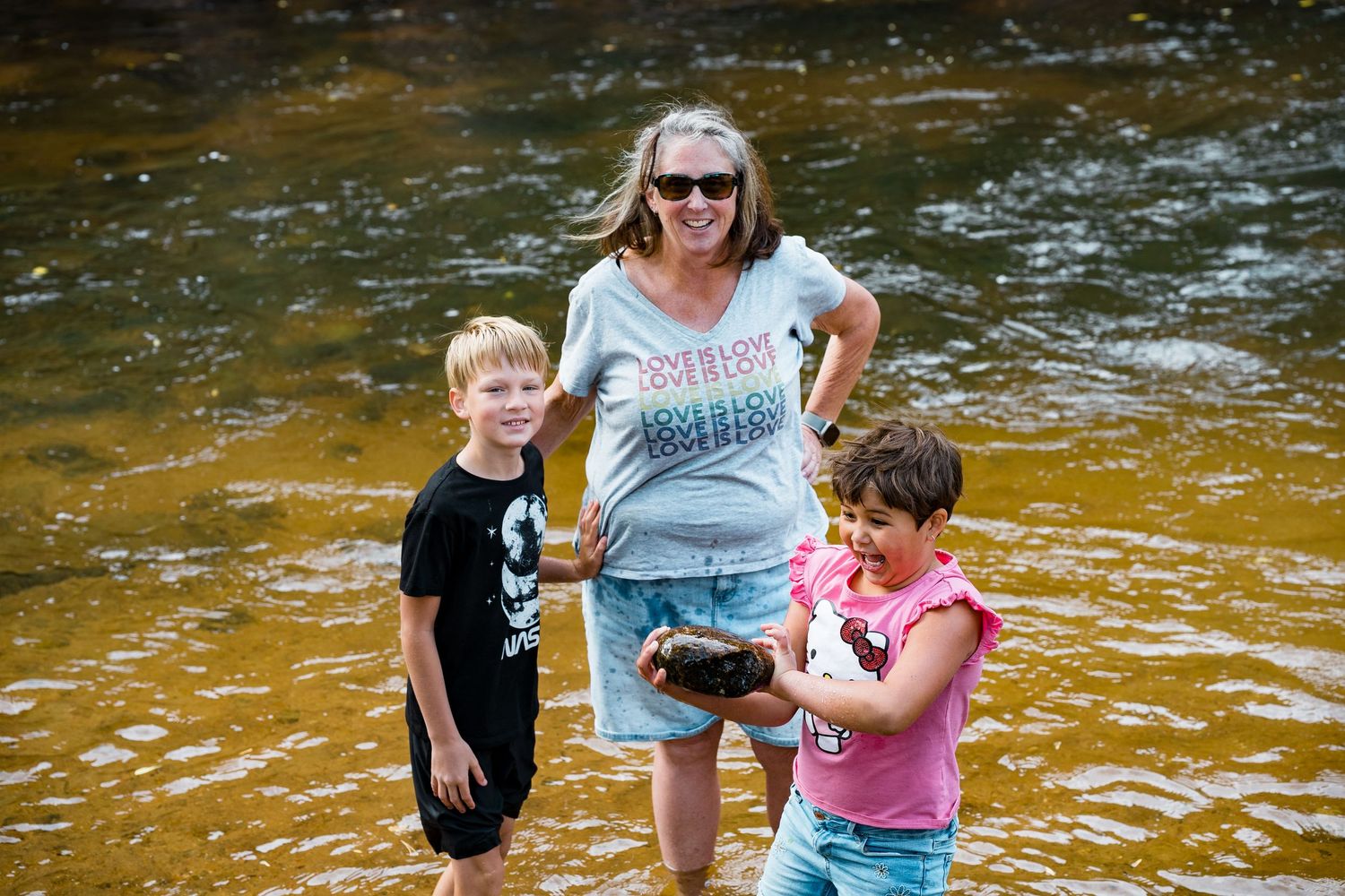 People enjoying a summer day splashing and playing in a shallow rocky stream with golden-brown water.