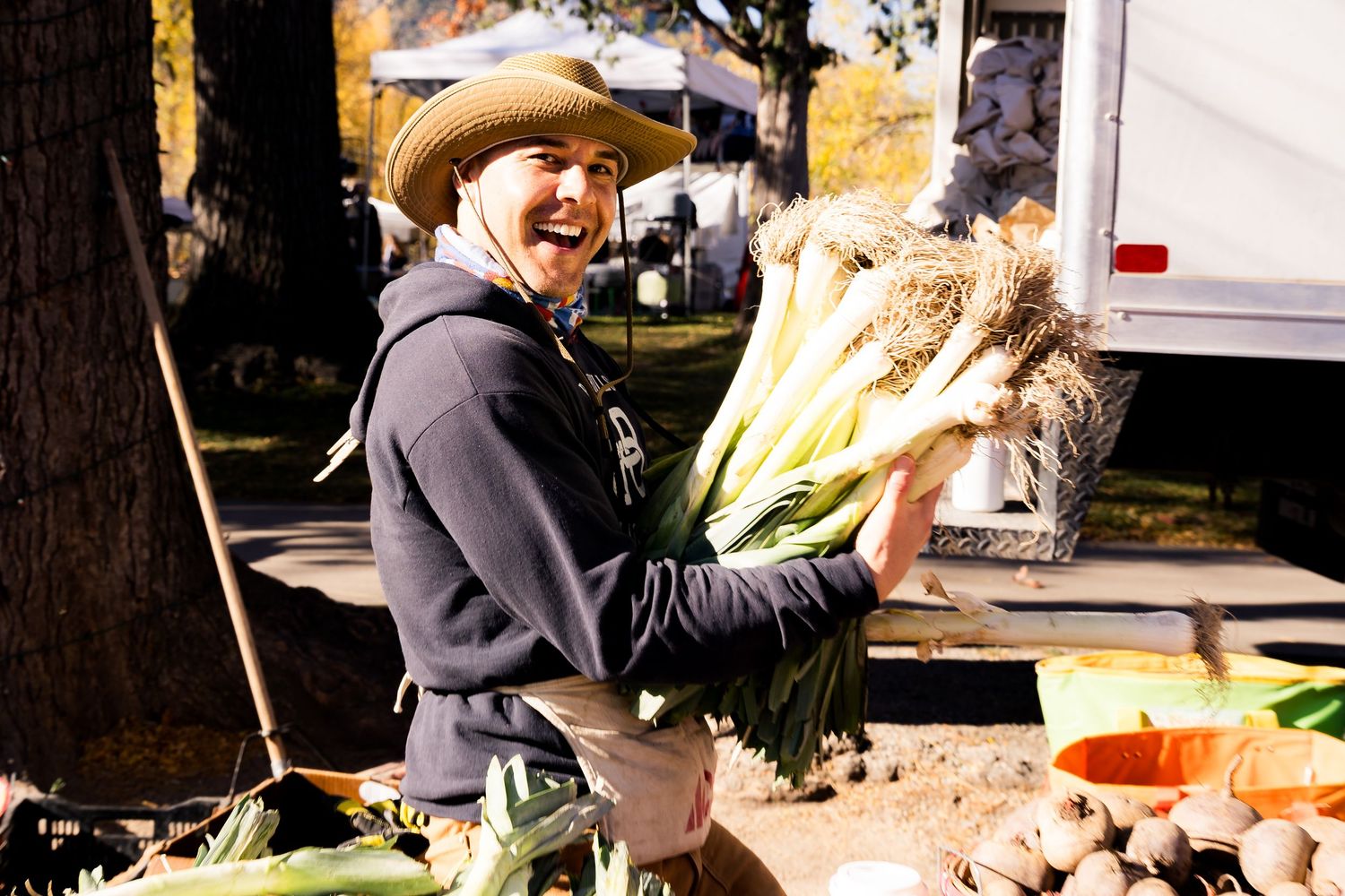Man smiling while holding green onion leafy greens at the Monroe Organic Farm booth at the farmers market.