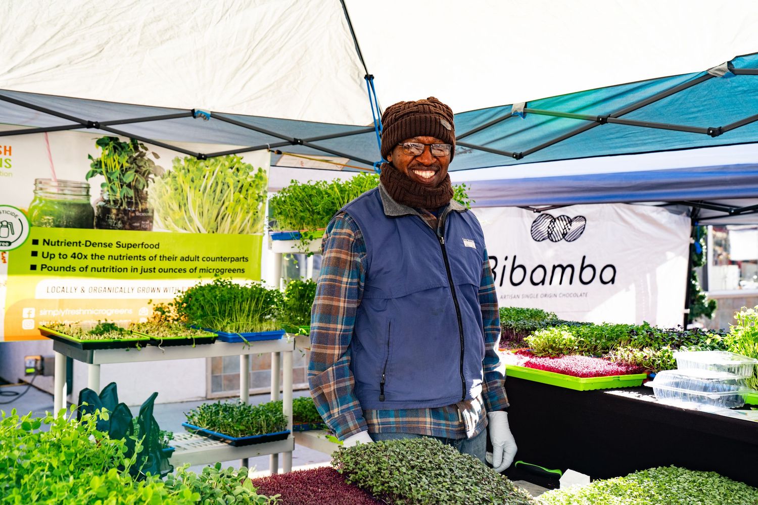 Vendor smiling proudly with a display of all his fresh microgreens at Boulder Farmers Market, locally grown Colorado produce.