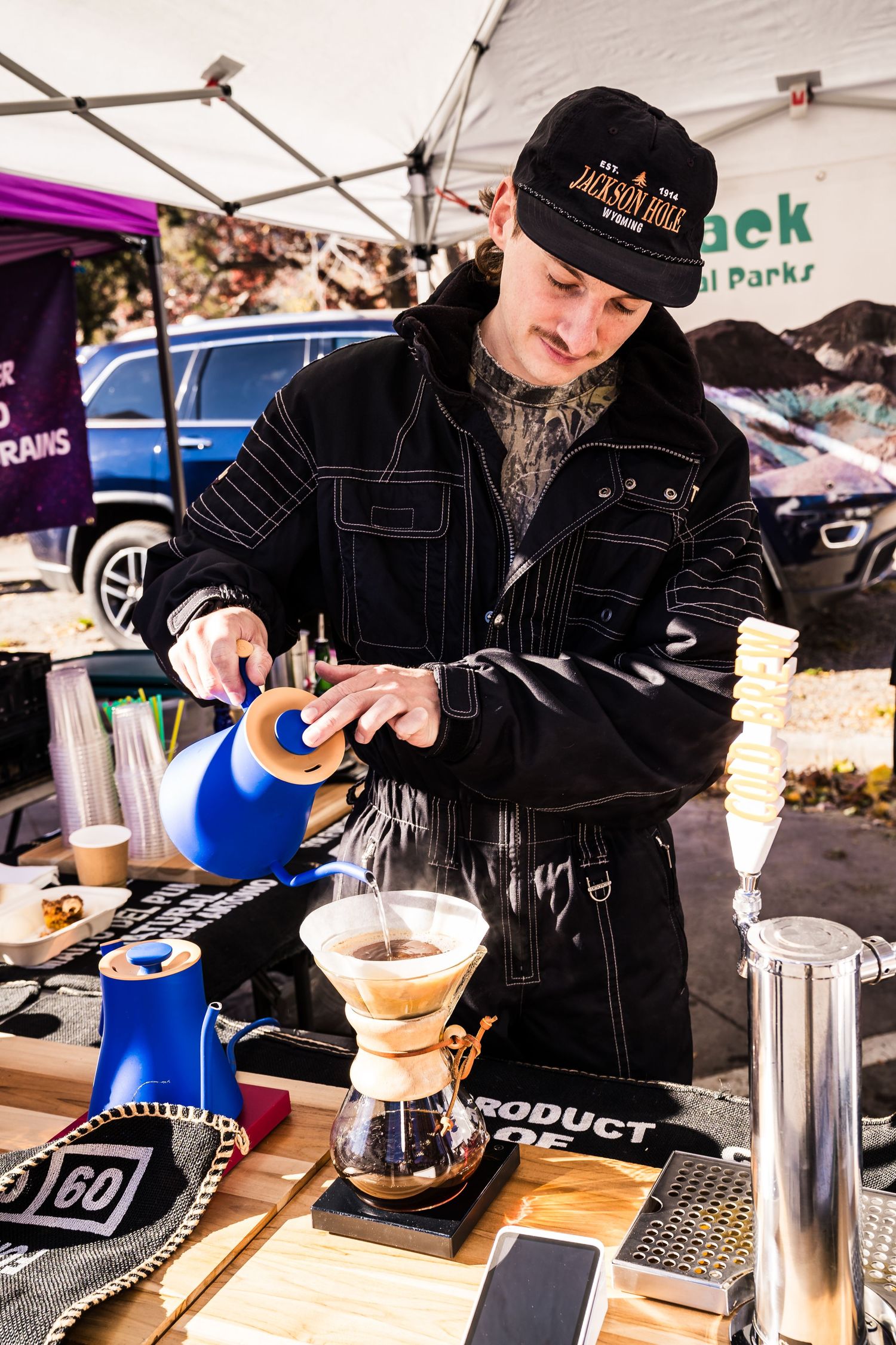 Barista pouring freshly brewed coffee at Park Pass Coffee booth, showcasing locally roasted Colorado beans at Boulder Farmers Market.