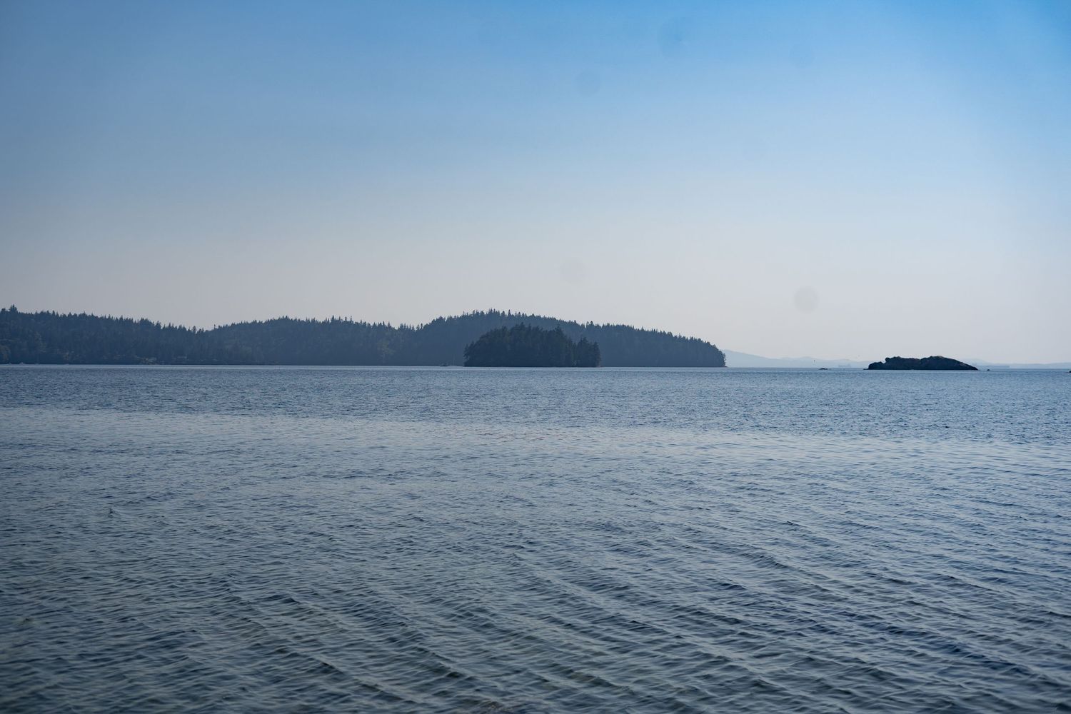 Calm blue ocean waters with tree-covered islands on the horizon under a clear sky.