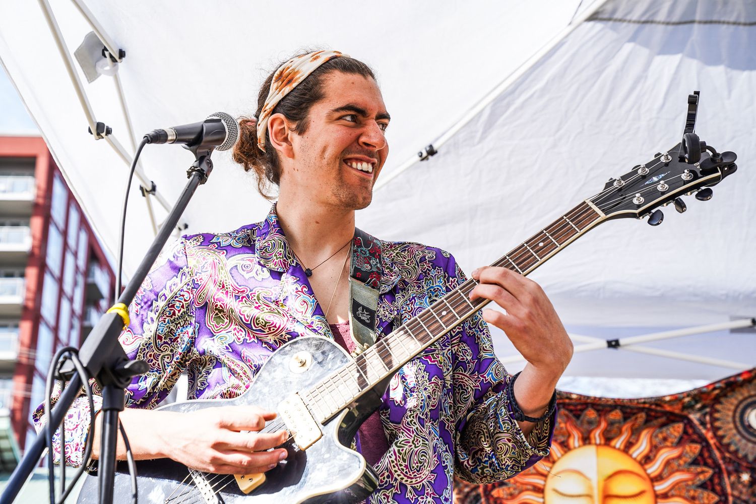 Musicians performing outdoors under white tent with guitars and instruments.