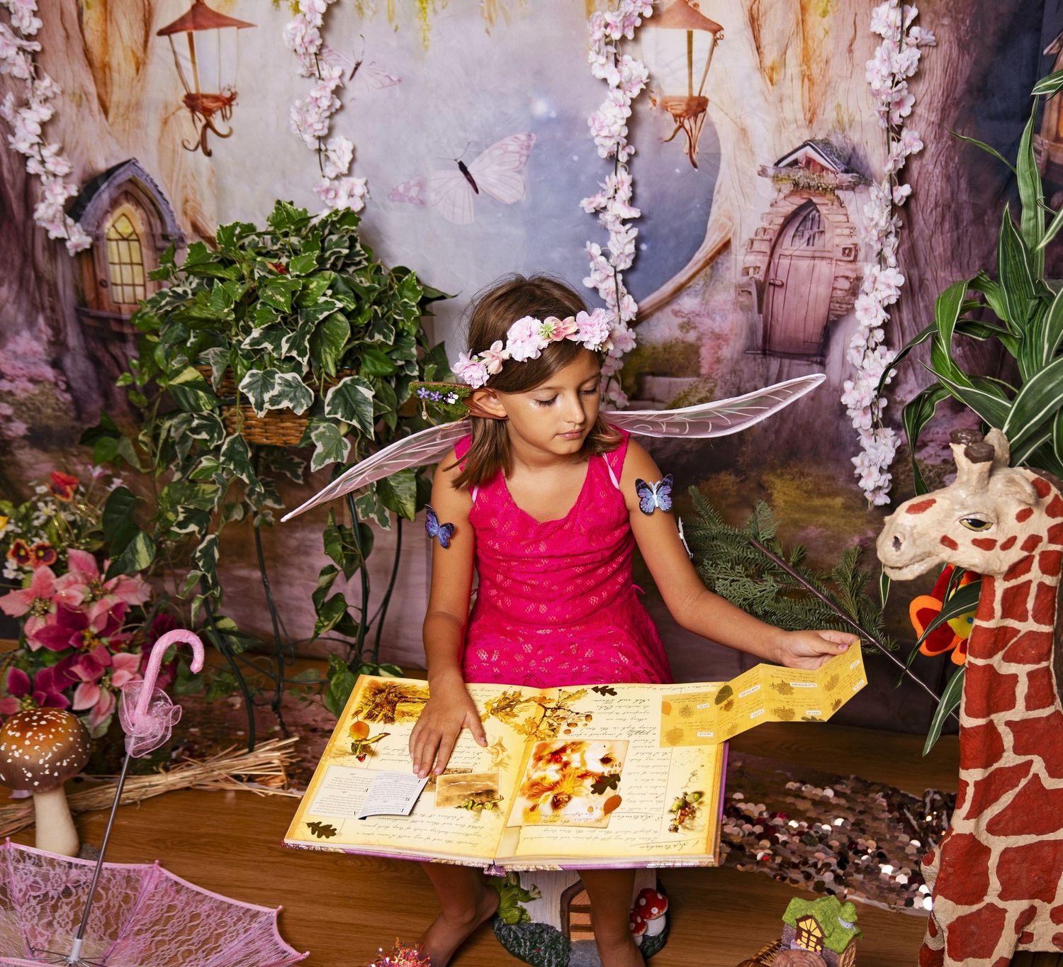 Young girl in fairy costume with wings reads a large book in an enchanted forest-themed fantasy setting.