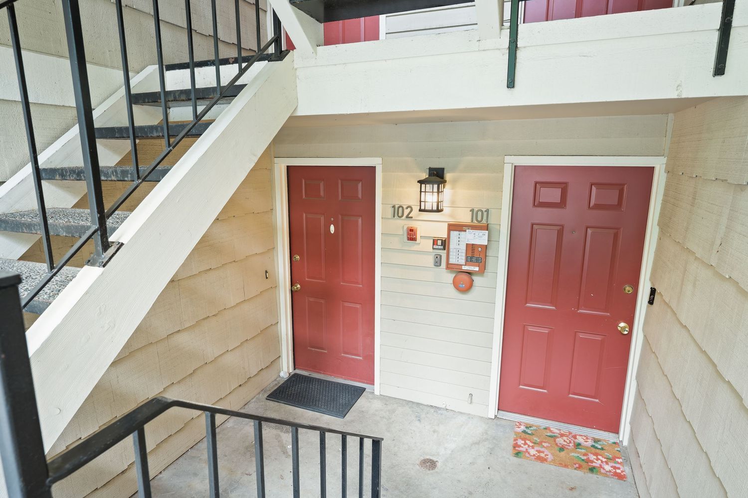 Two red apartment doors numbered 102 and 101 beneath an exterior staircase with black metal railings.