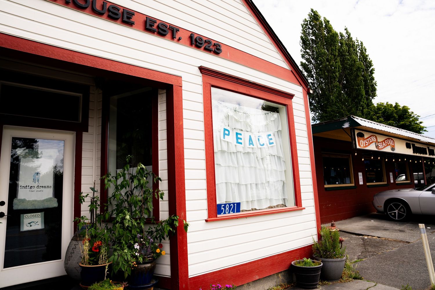 Exterior of a vintage white and red building established in 1925 with a Peace sign in the window and potted plants.