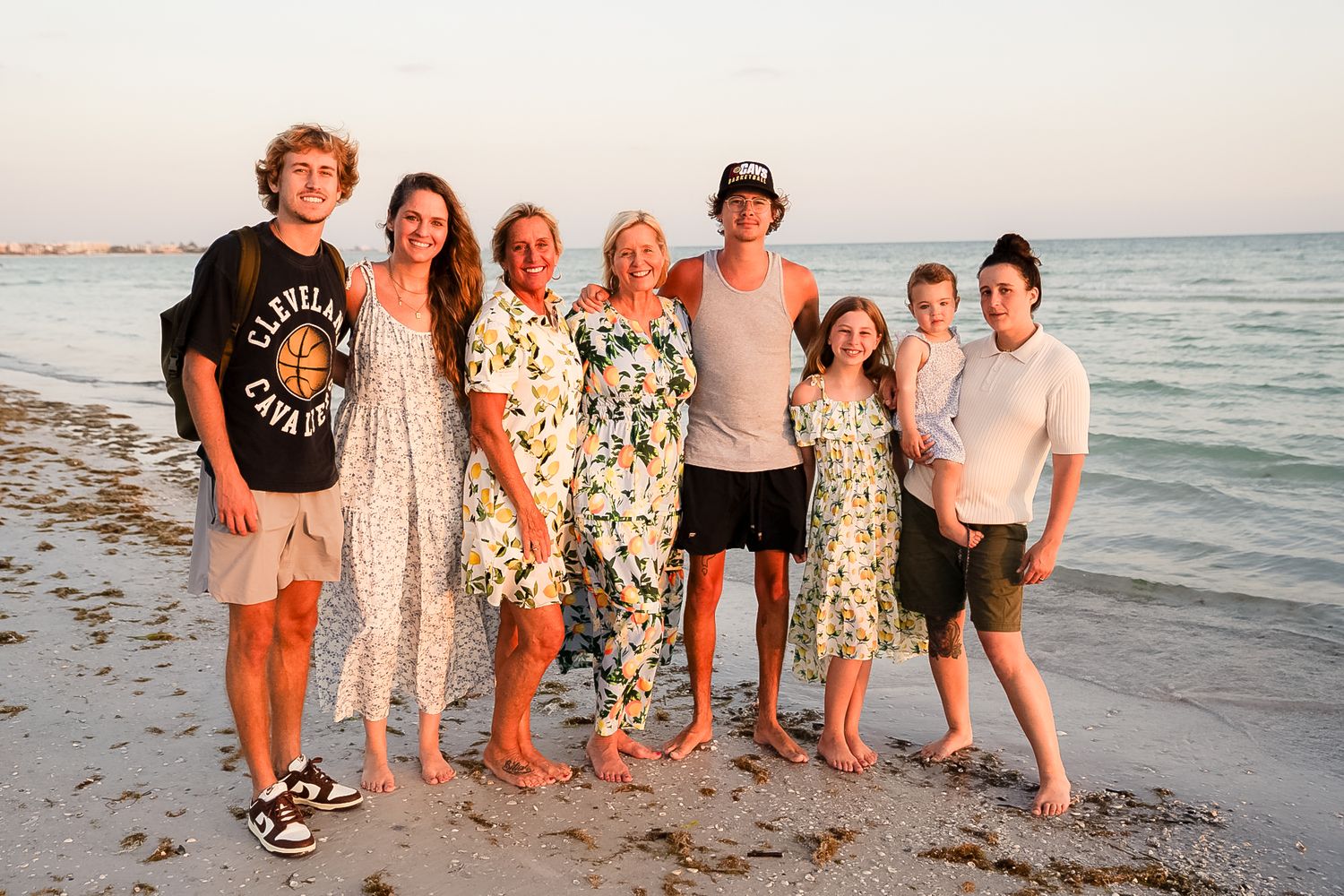A photo of all the family members and the ocean behind them and the rainbow sky.