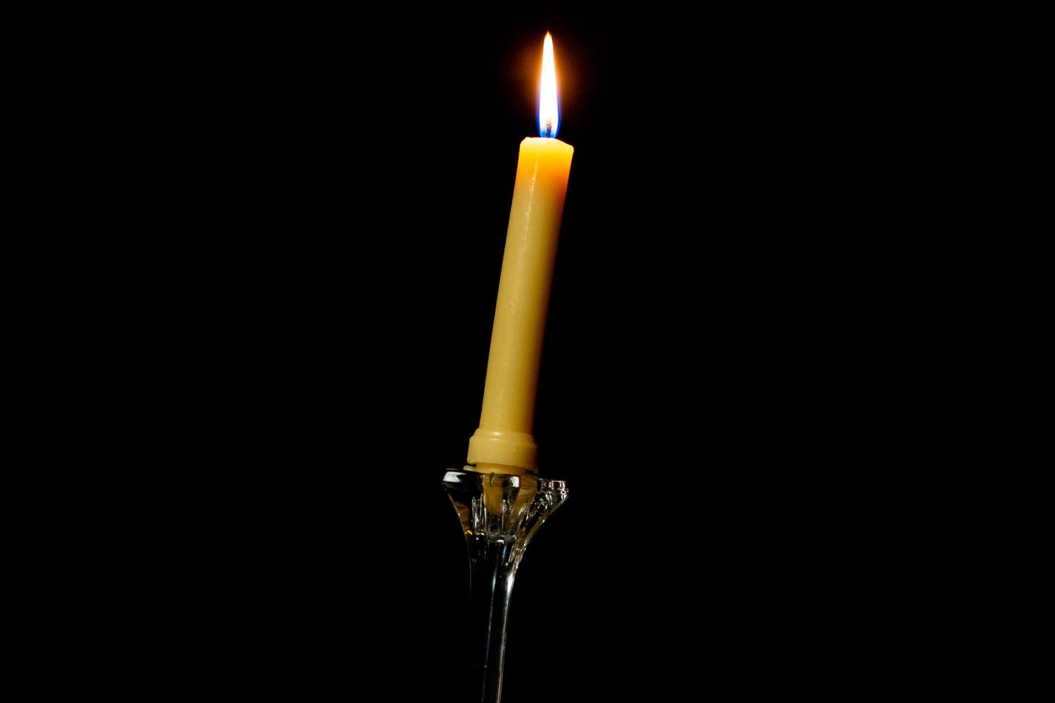 A burning candle with a bright flame on a dark background showing different stages of melting.