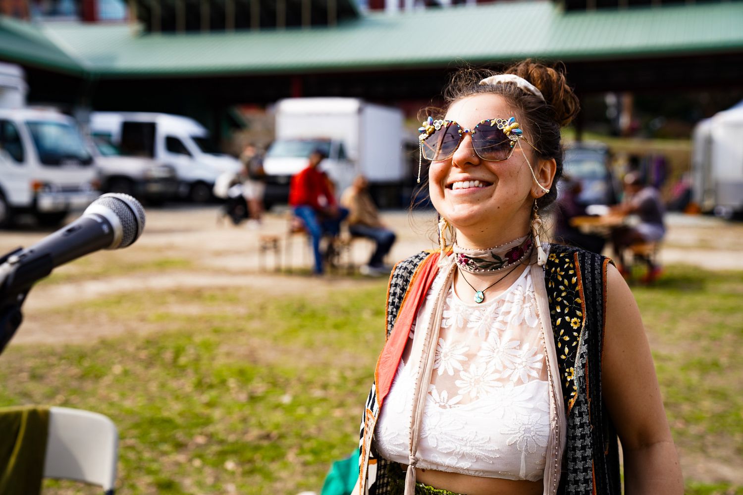 A woman wearing a colorful vest, bright glasses, and earrings smiles while dressed in a silk white top in downtown Boulder