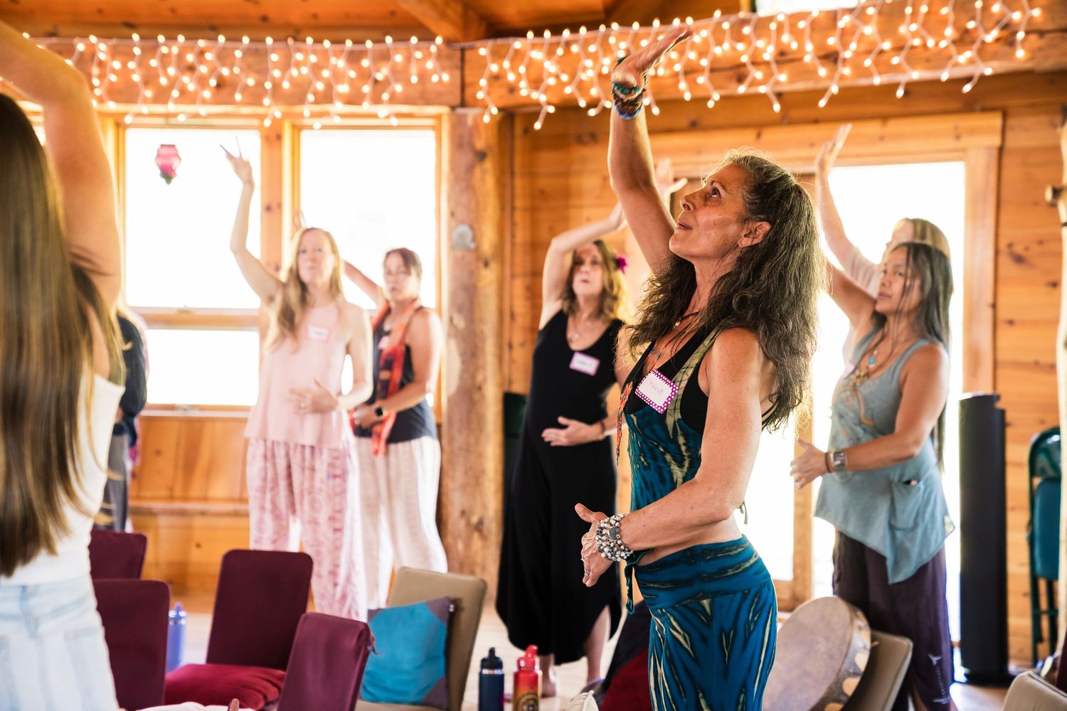 A group of people dancing and socializing in a rustic wooden cabin decorated with string lights.