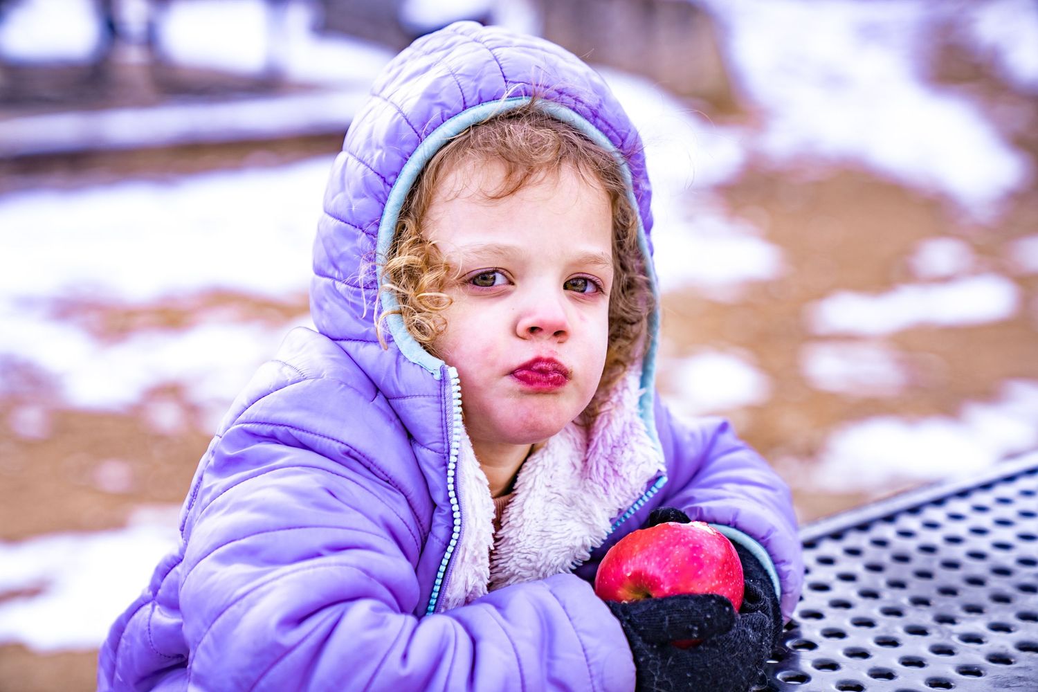 A child in a purple winter coat and knit hat plays outdoors in the snow.