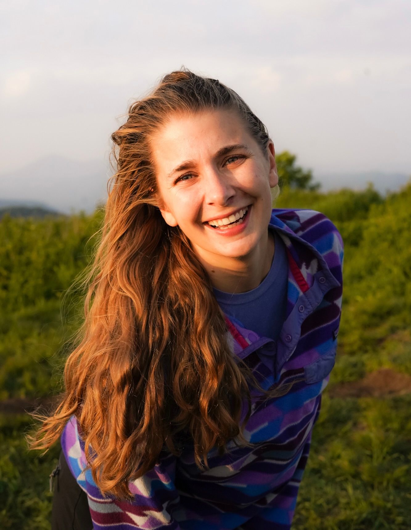 A woman with long, wavy blonde hair laughing and smiling at the camera, bathed in warm golden light.