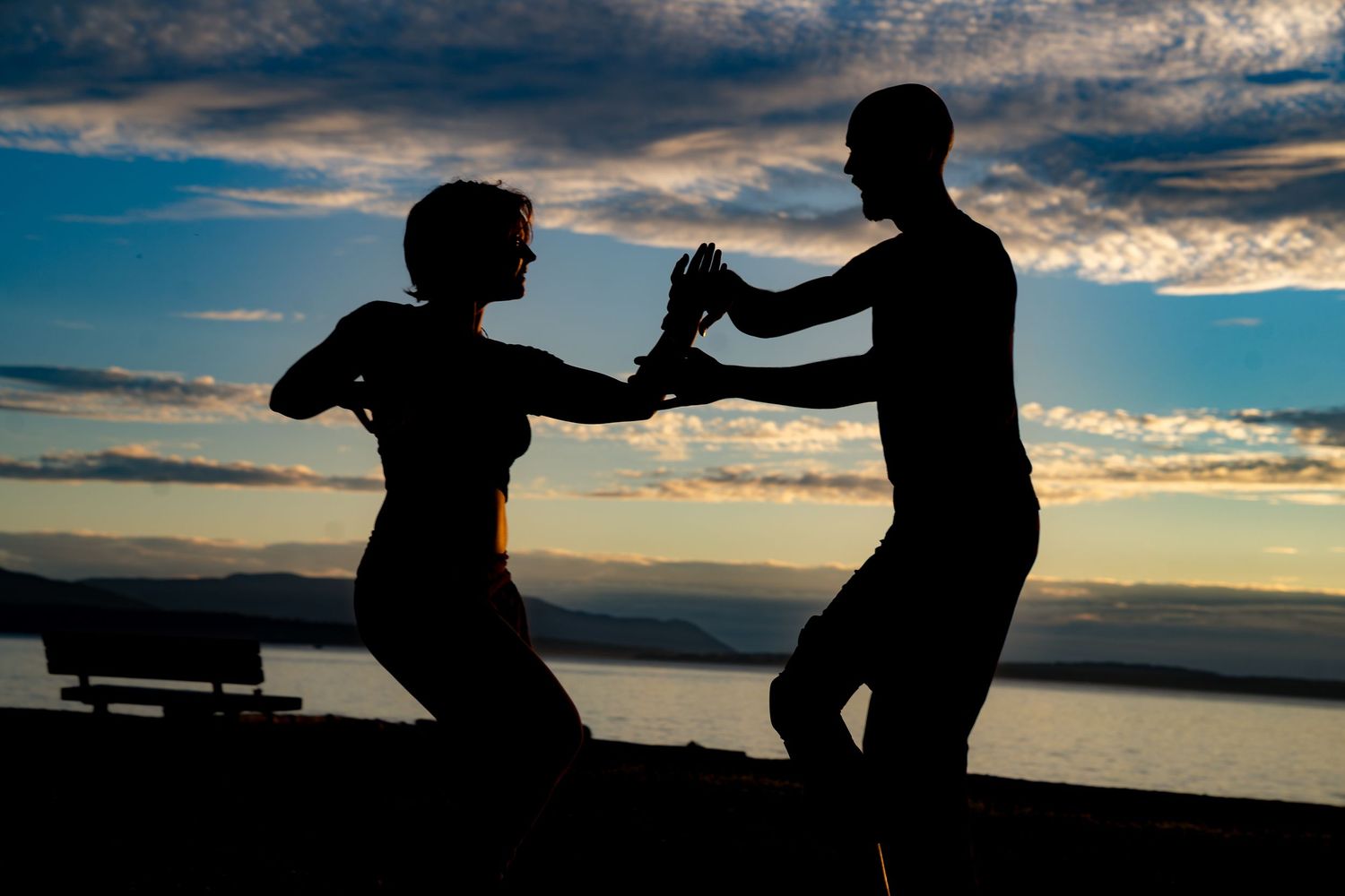 Silhouette of a couple dancing at sunset by the water with a dramatic cloudy sky backdrop.