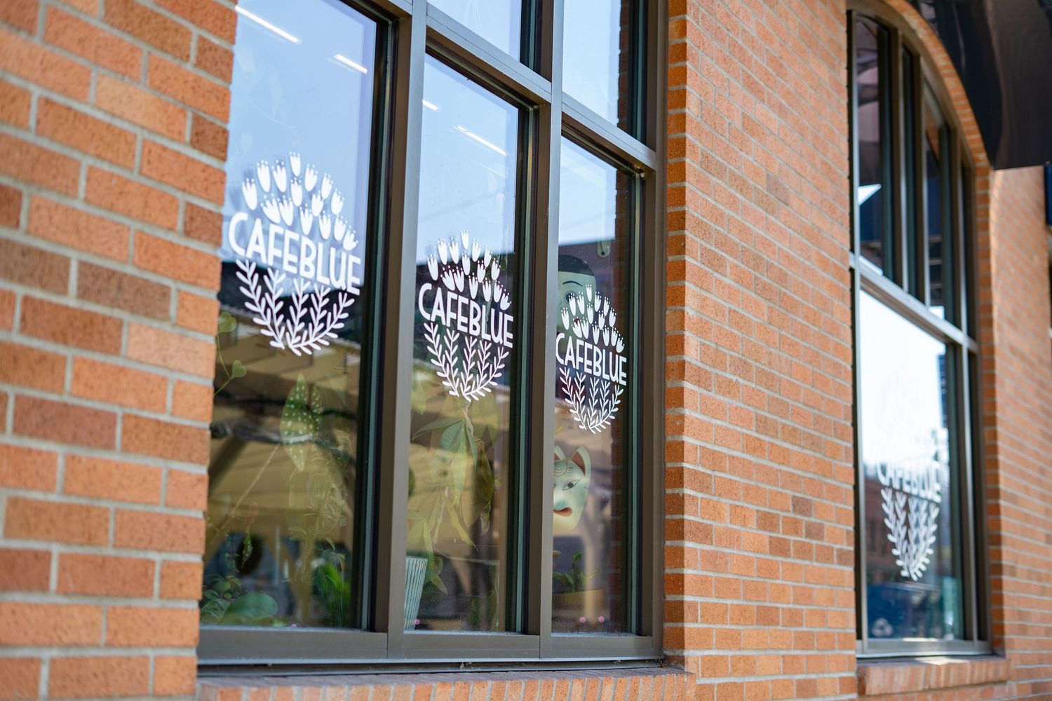 Brick building exterior with black-framed windows displaying Cafe Blue logo decals with wheat wreath design.