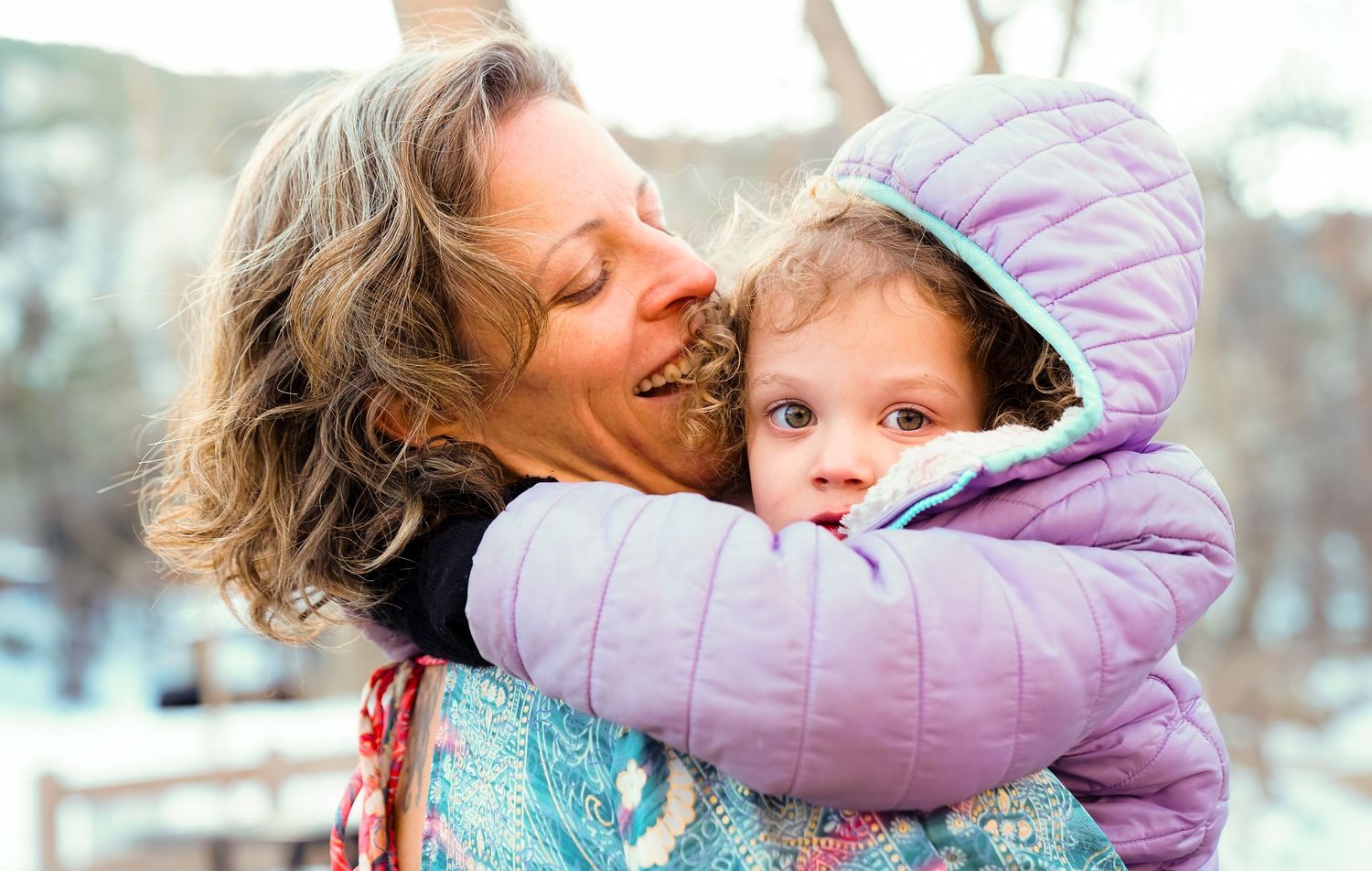 A loving embrace between two people outdoors in winter with snow visible in the background.