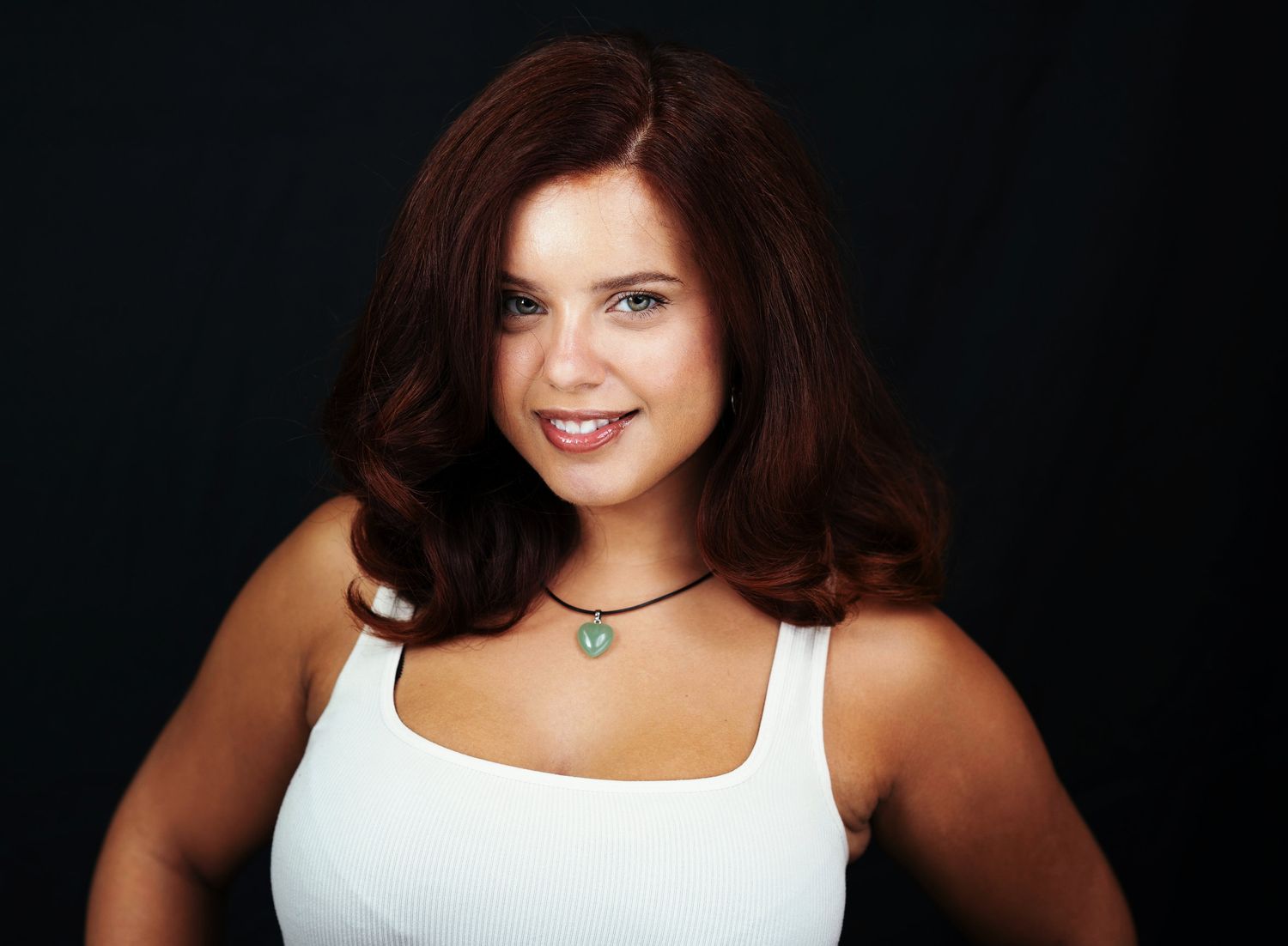 A woman is smiling at the camera, she has medium length brown hair and is smiling at the camera.
