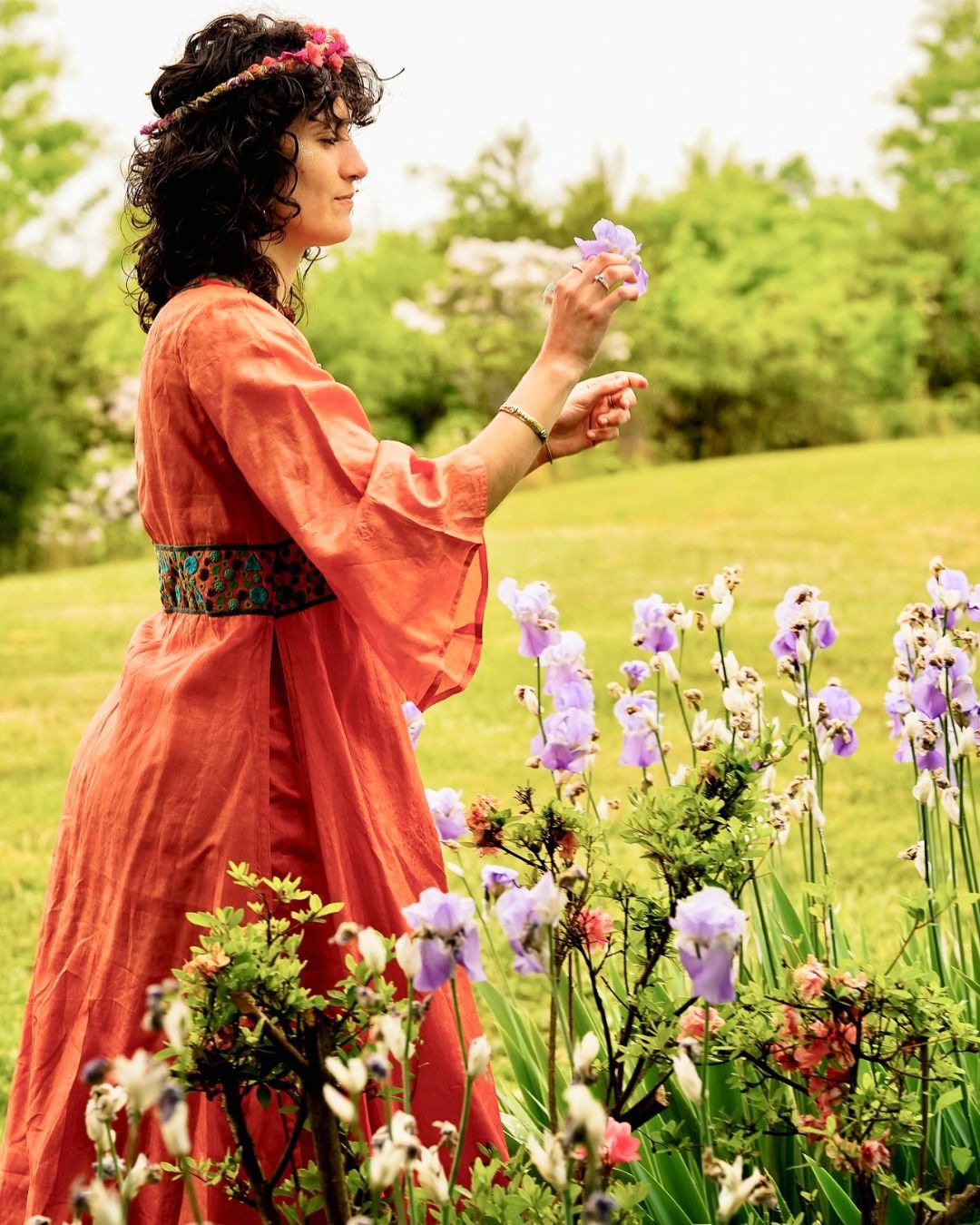 Woman in orange dress picking purple iris flowers in garden.
