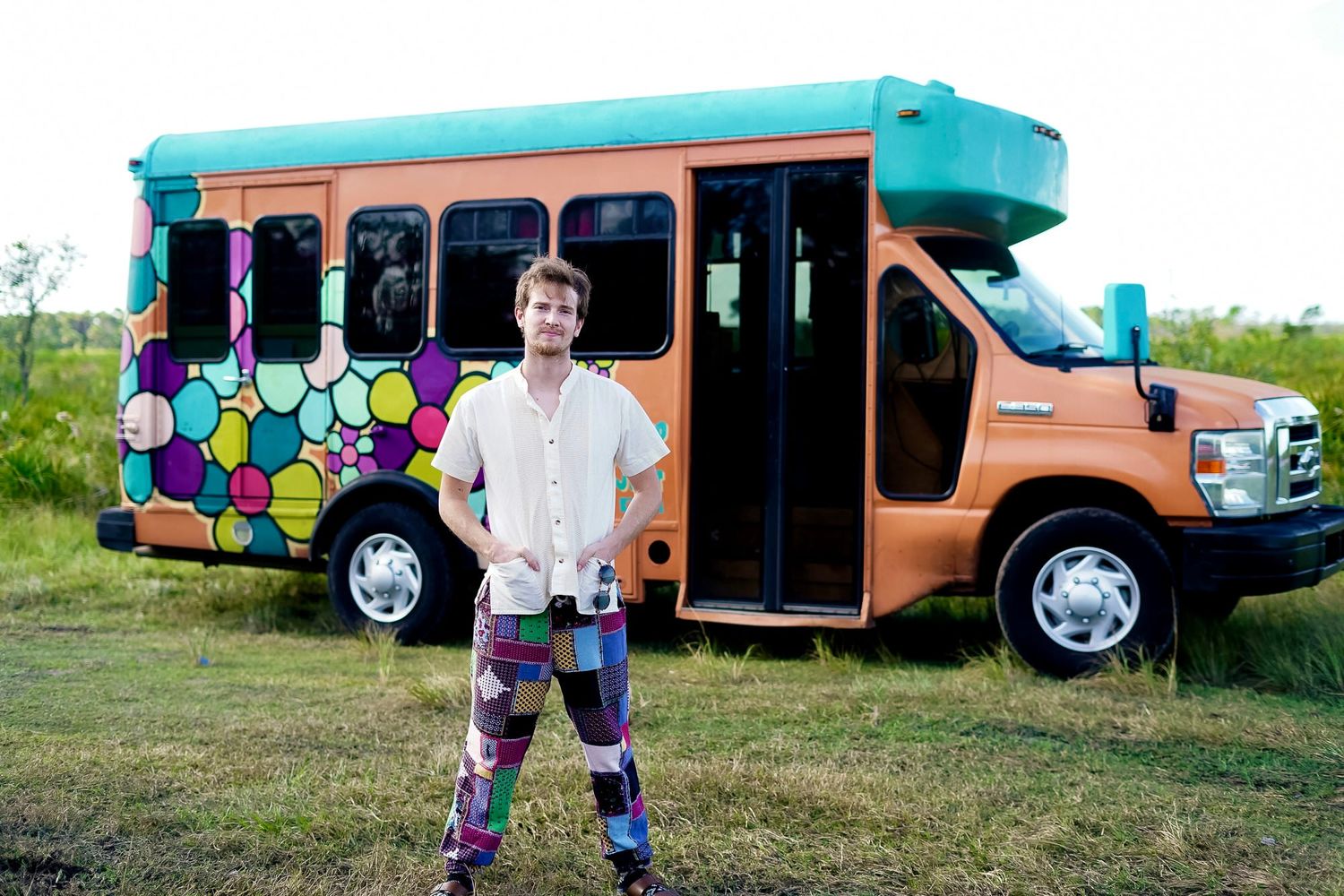 Person standing in front of a colorful painted orange bus with vibrant floral designs outdoors.