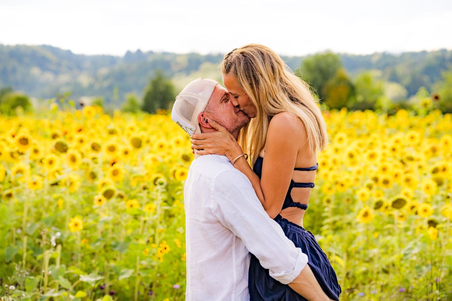 Couple sharing a romantic kiss in a vibrant sunflower field on a sunny day.