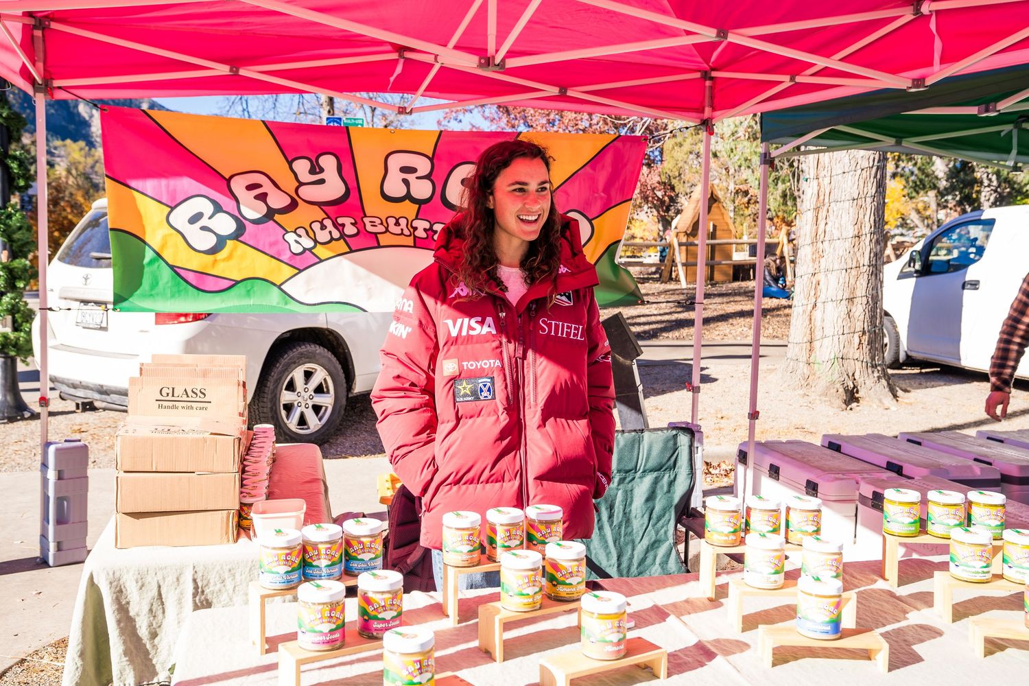 Woman at the Ray Road Nut Butter booth smiling and engaging with a customer at the farmers market.