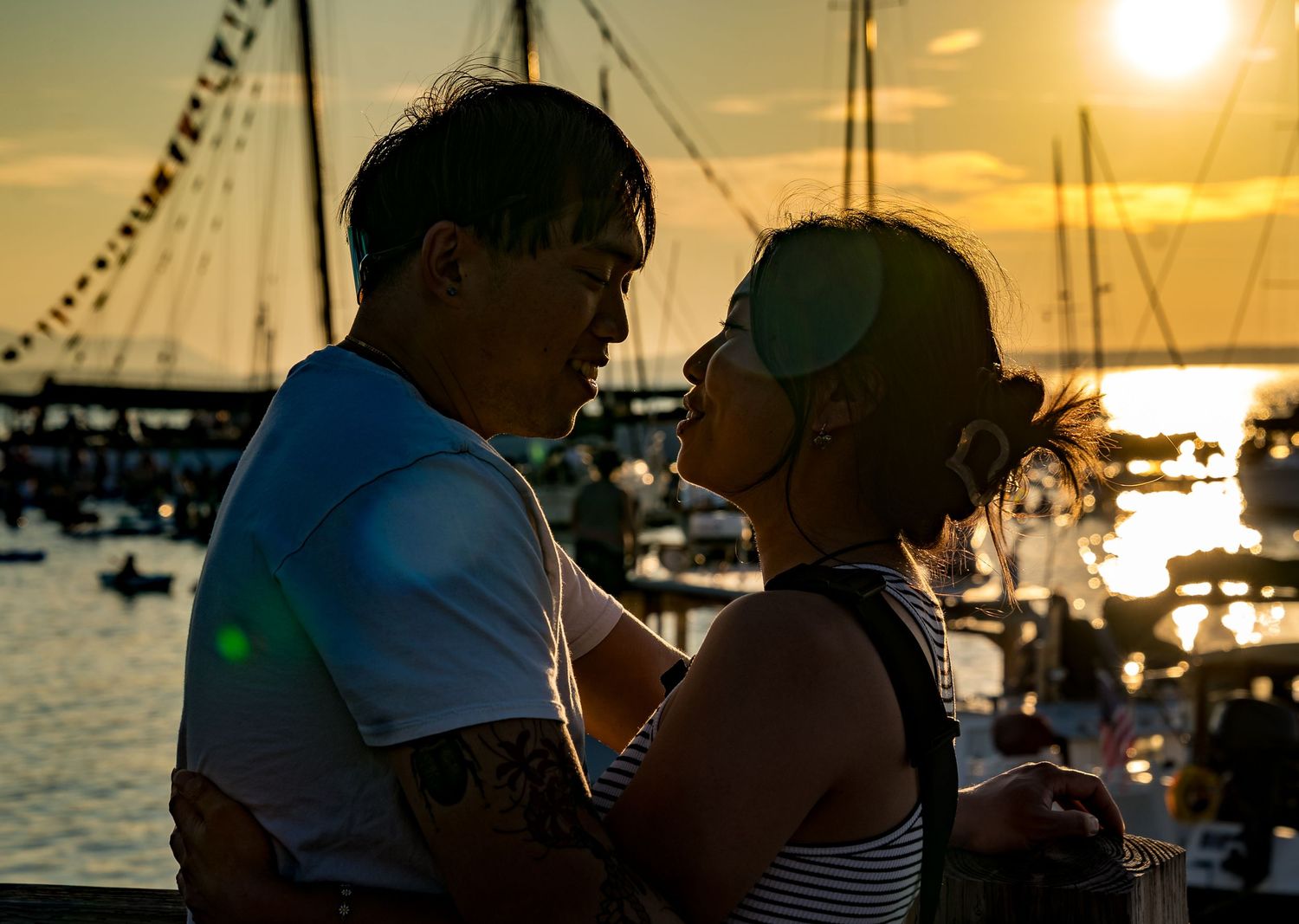 Couple sharing a romantic moment at sunset by a marina with sailboats in the golden background.