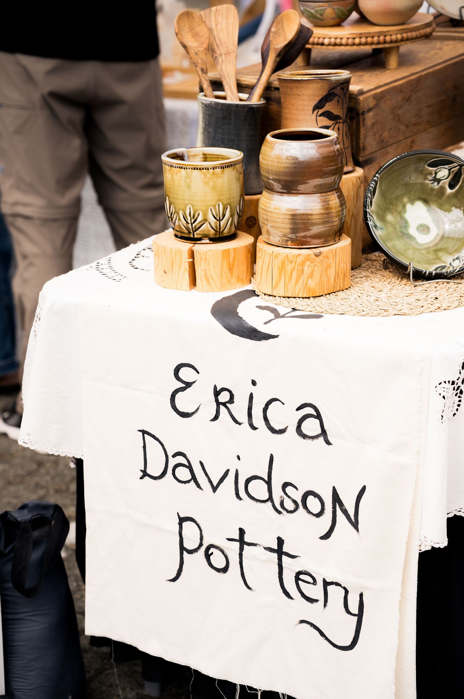 Erica Davidson Pottery display table with handmade ceramic mugs and bowls at an outdoor craft market.