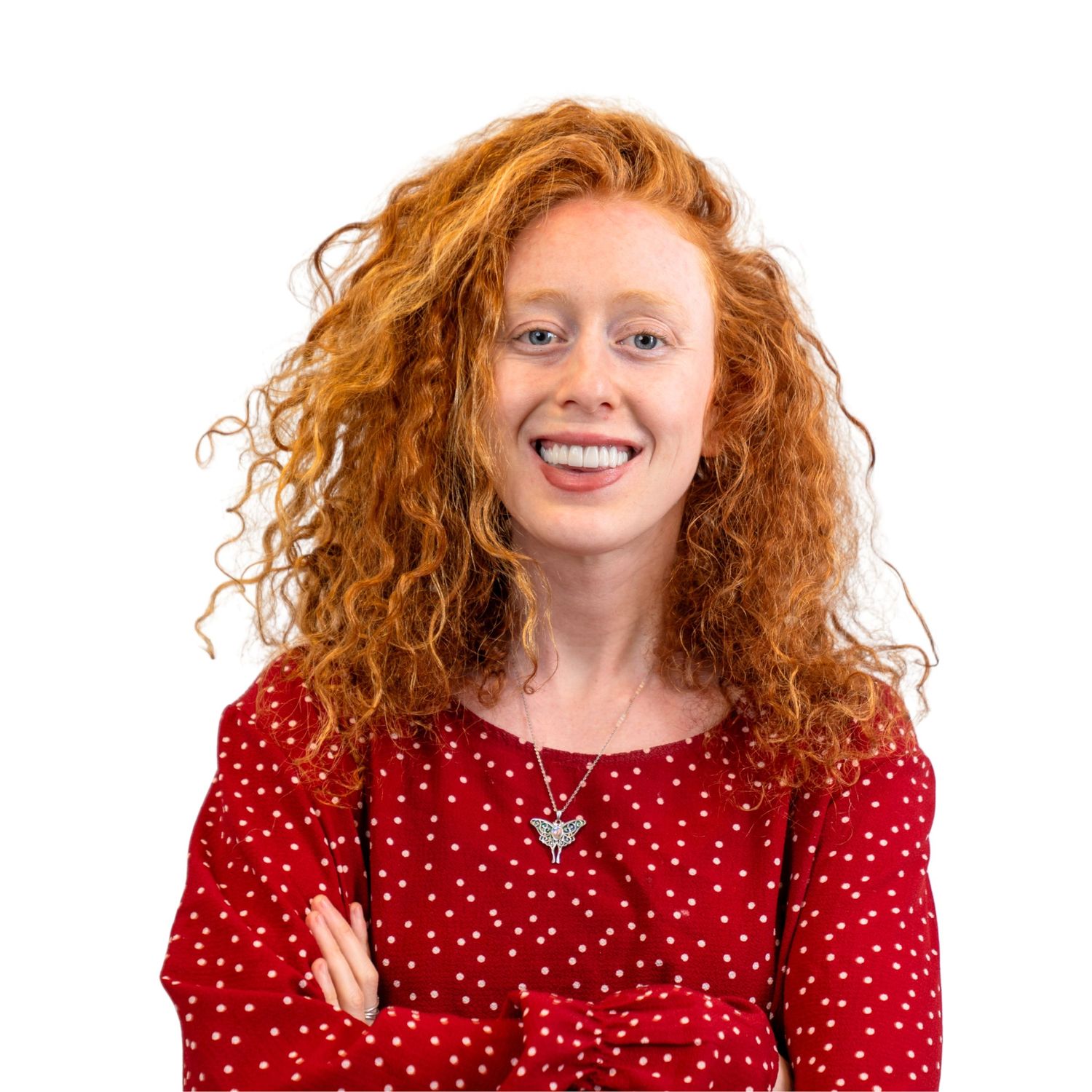 A self portrait of Jessie with curly orange hair wearing a red dress with white polka dots, smiling at the camera.