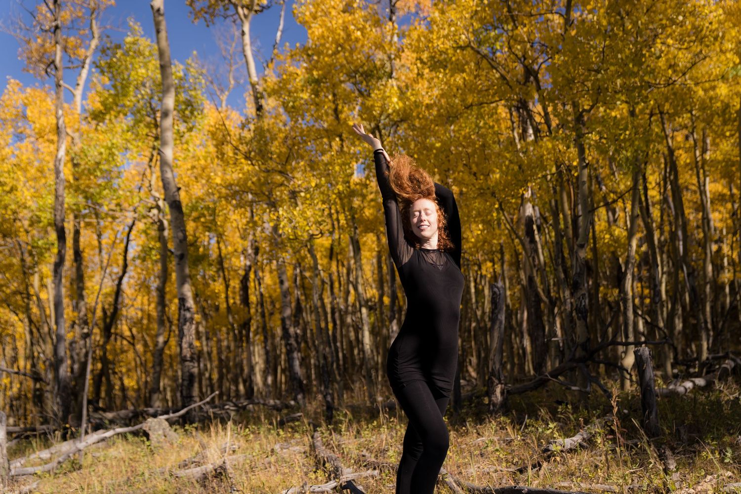Self-portrait of Jessie Greenberg standing in the woods surrounded by beautiful autumn leaves. Natural light filters through the trees, high