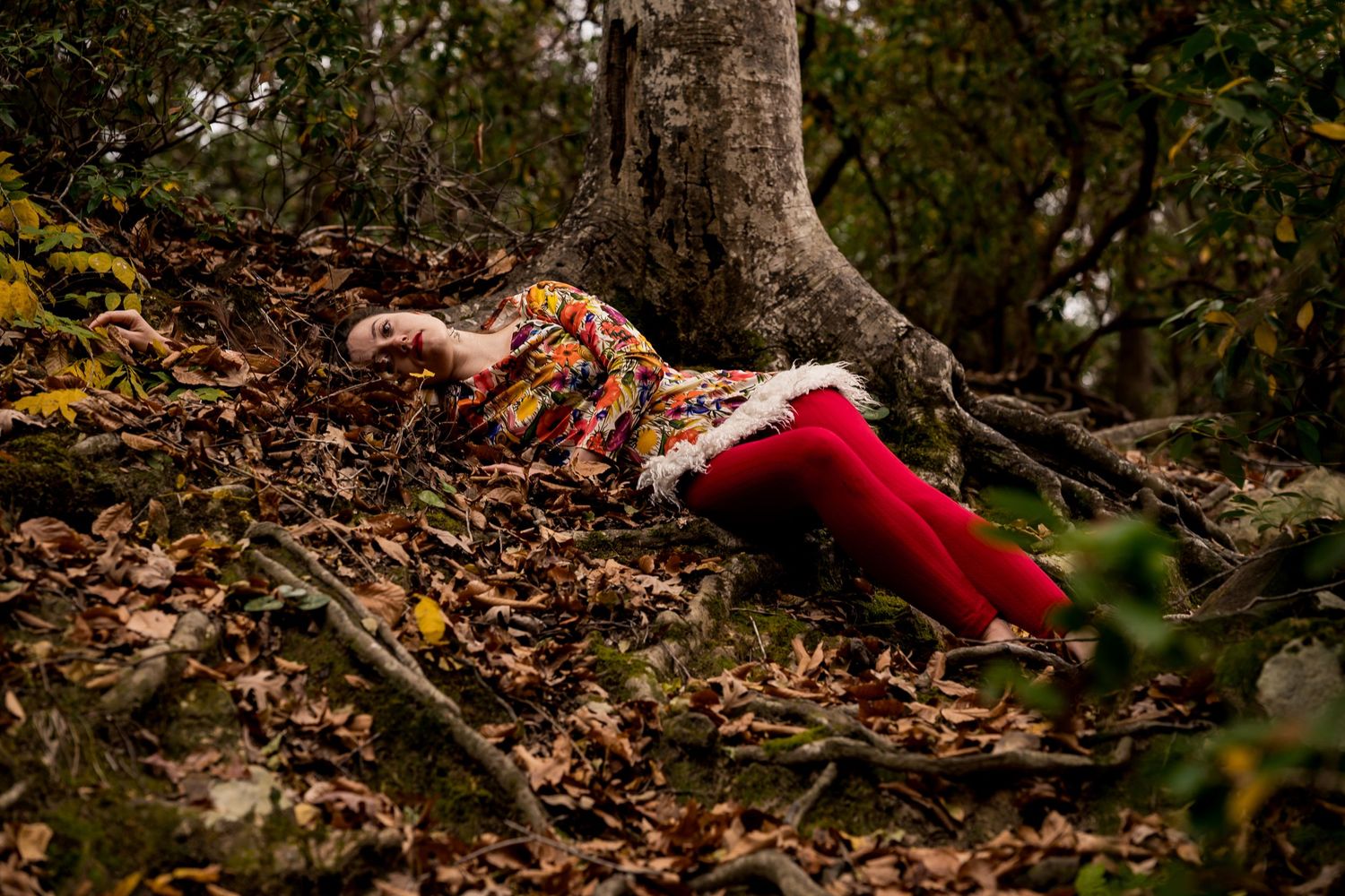 A person in red clothing lies on autumn leaves in a forest setting during a creative outdoor photoshoot.