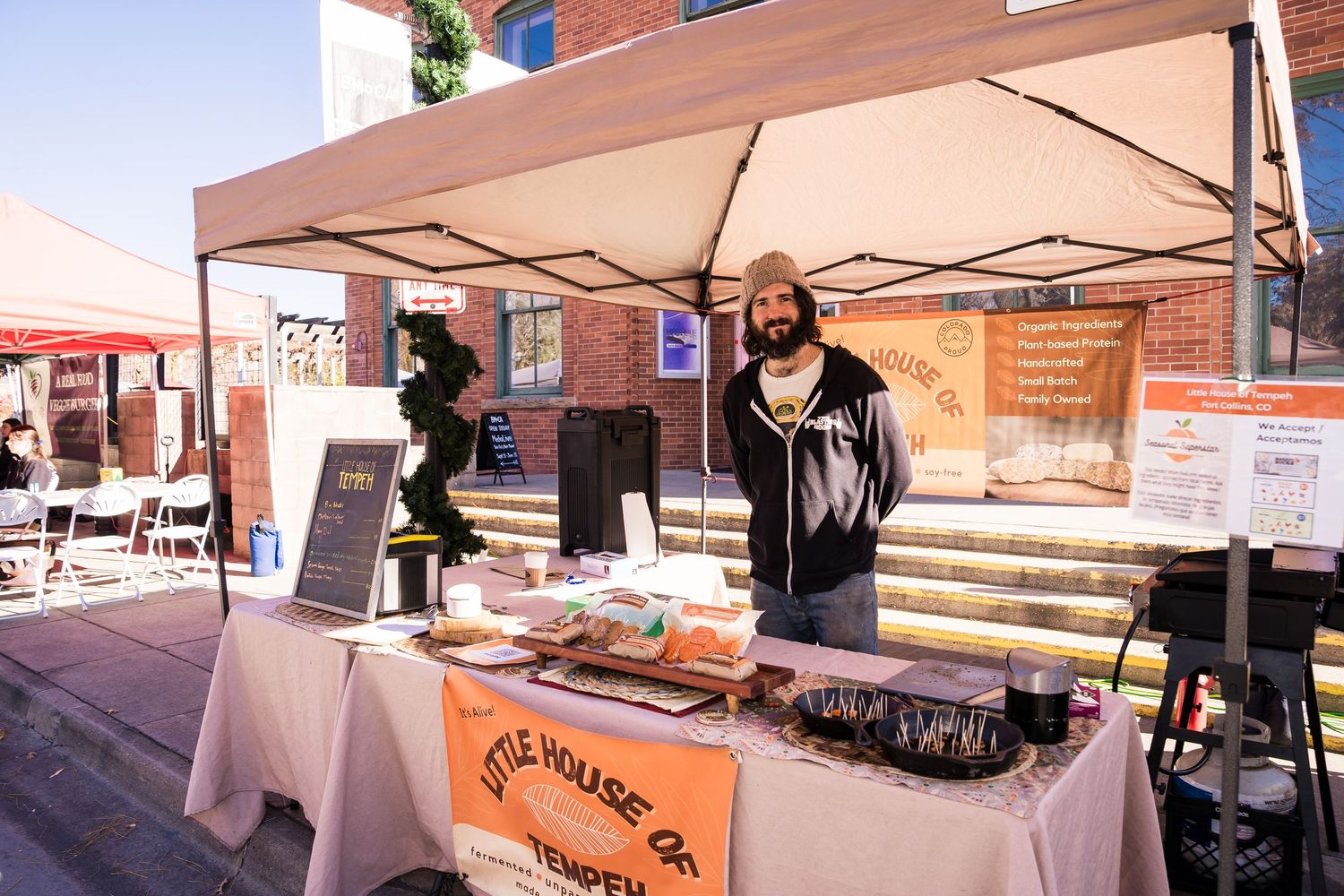 Man at The Little House of Tempeh booth smiling at the camera at the farmers market.
