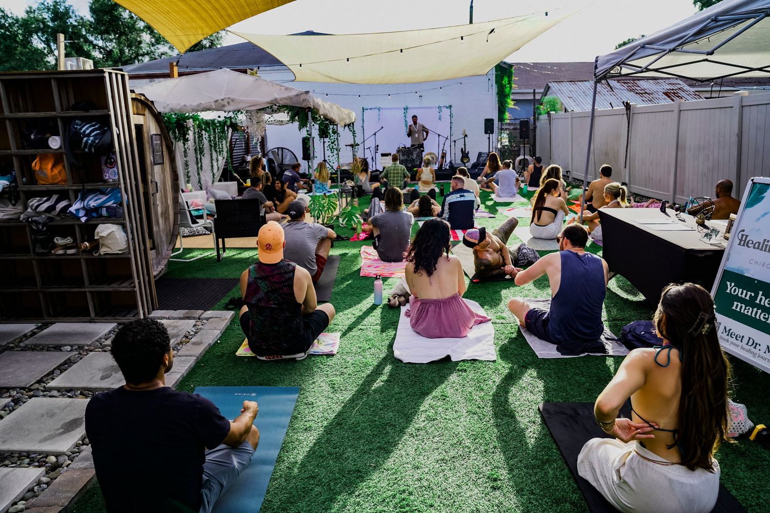 A photo of all people sitting on their yoga mats looking at the stage going to do yoga.