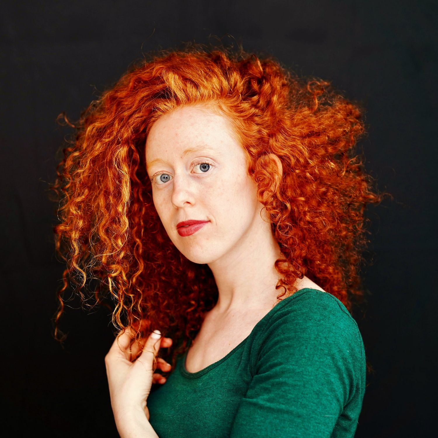 A self portrait of jessie with orange curly hair and wearing a green top.