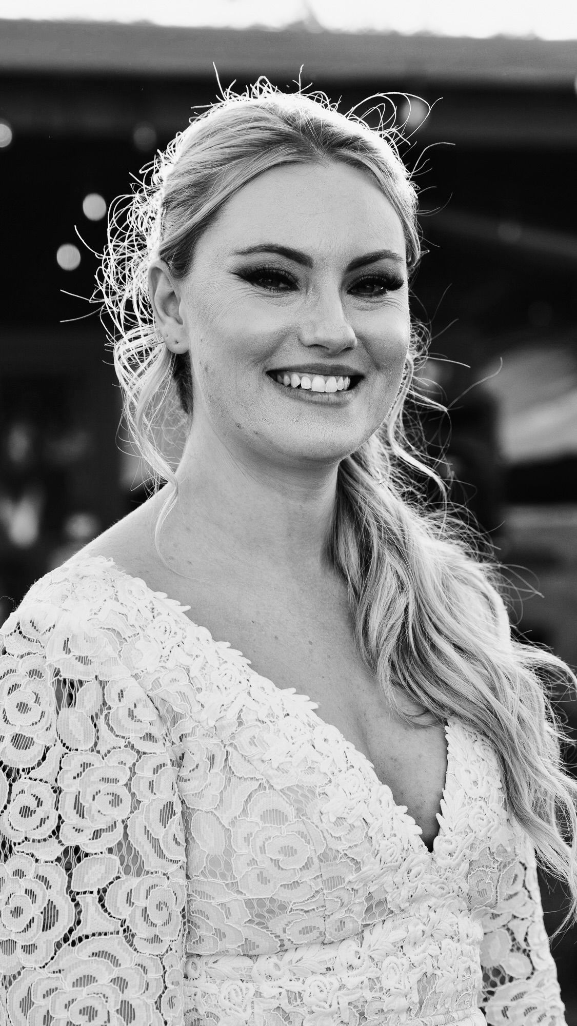 Smiling blonde woman in a white lace dress posing for a black and white portrait photo.