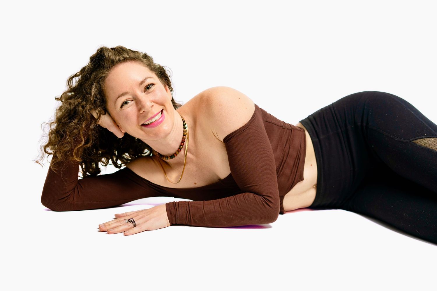 Woman in brown top lying down on white background during professional photo shoot.