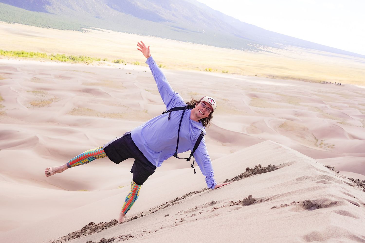 A photo of a guy doing a sideways yoga pose, he is wearing a hat, wearing a light blue sweater, he is also wearing geometric leggings.