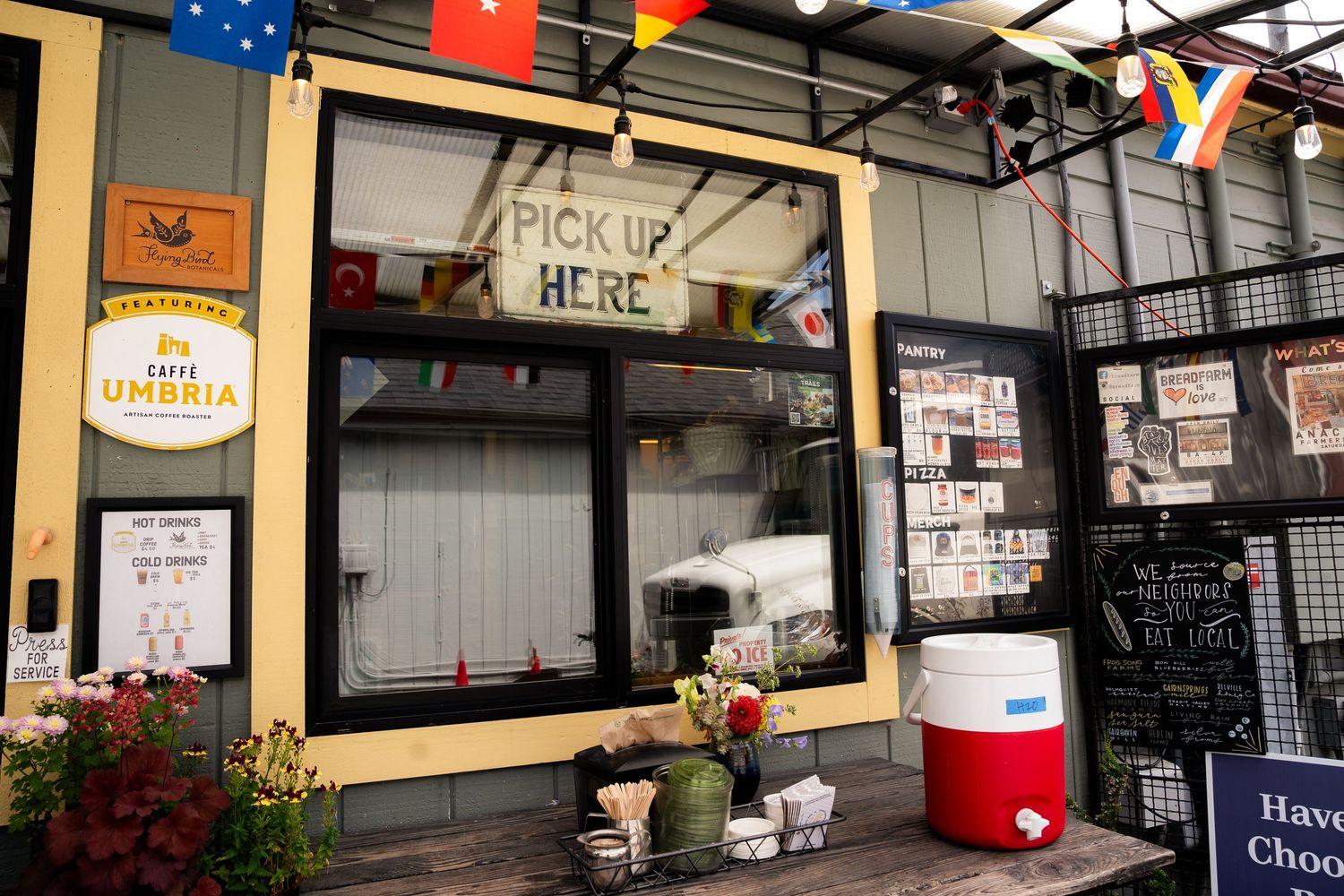 Caffe Umbria pick-up window at an outdoor coffee kiosk with colorful flags and a red cooler.