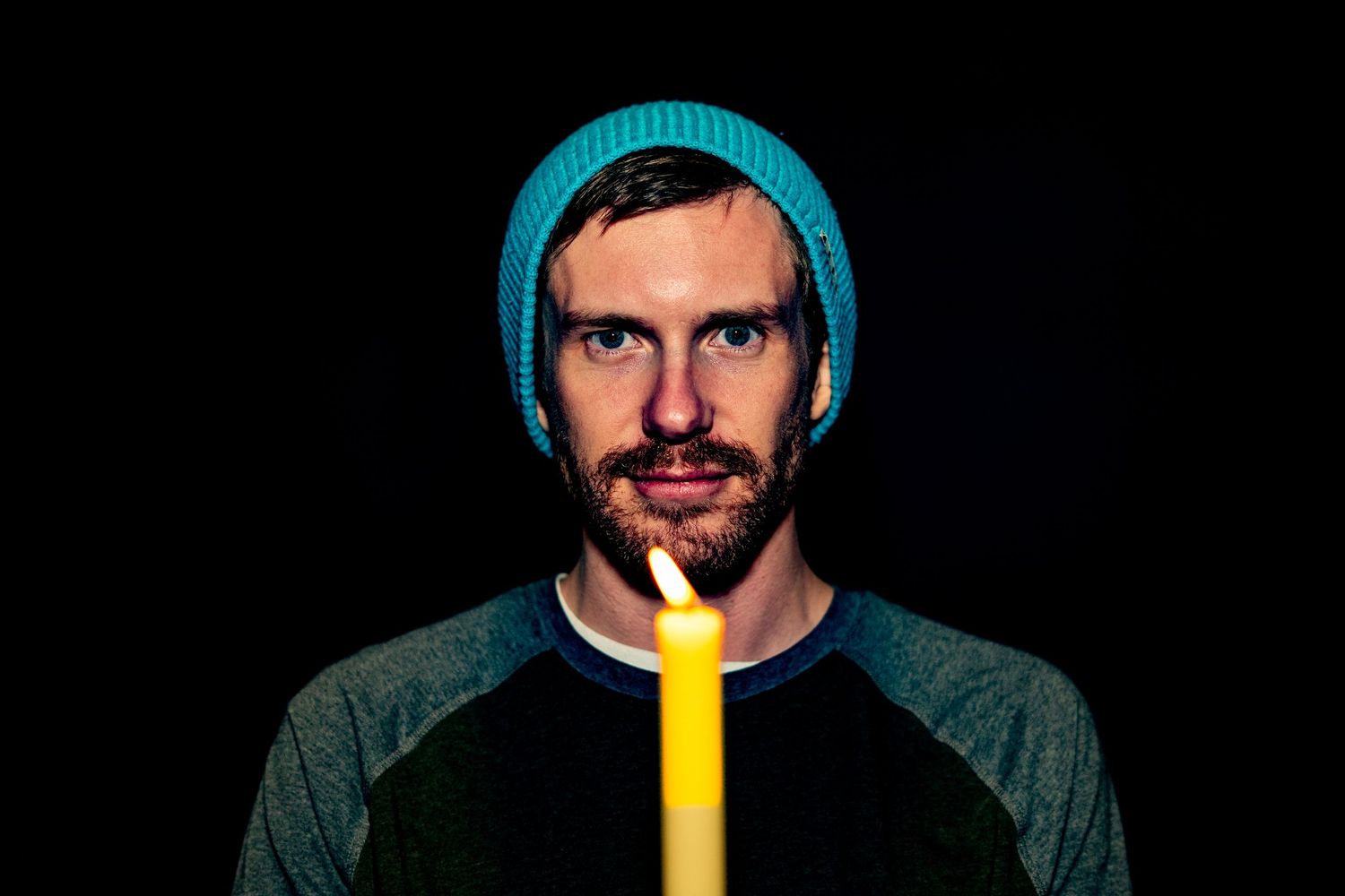 A person wearing a blue beanie holds a yellow glowing light stick in their mouth against a dark background.
