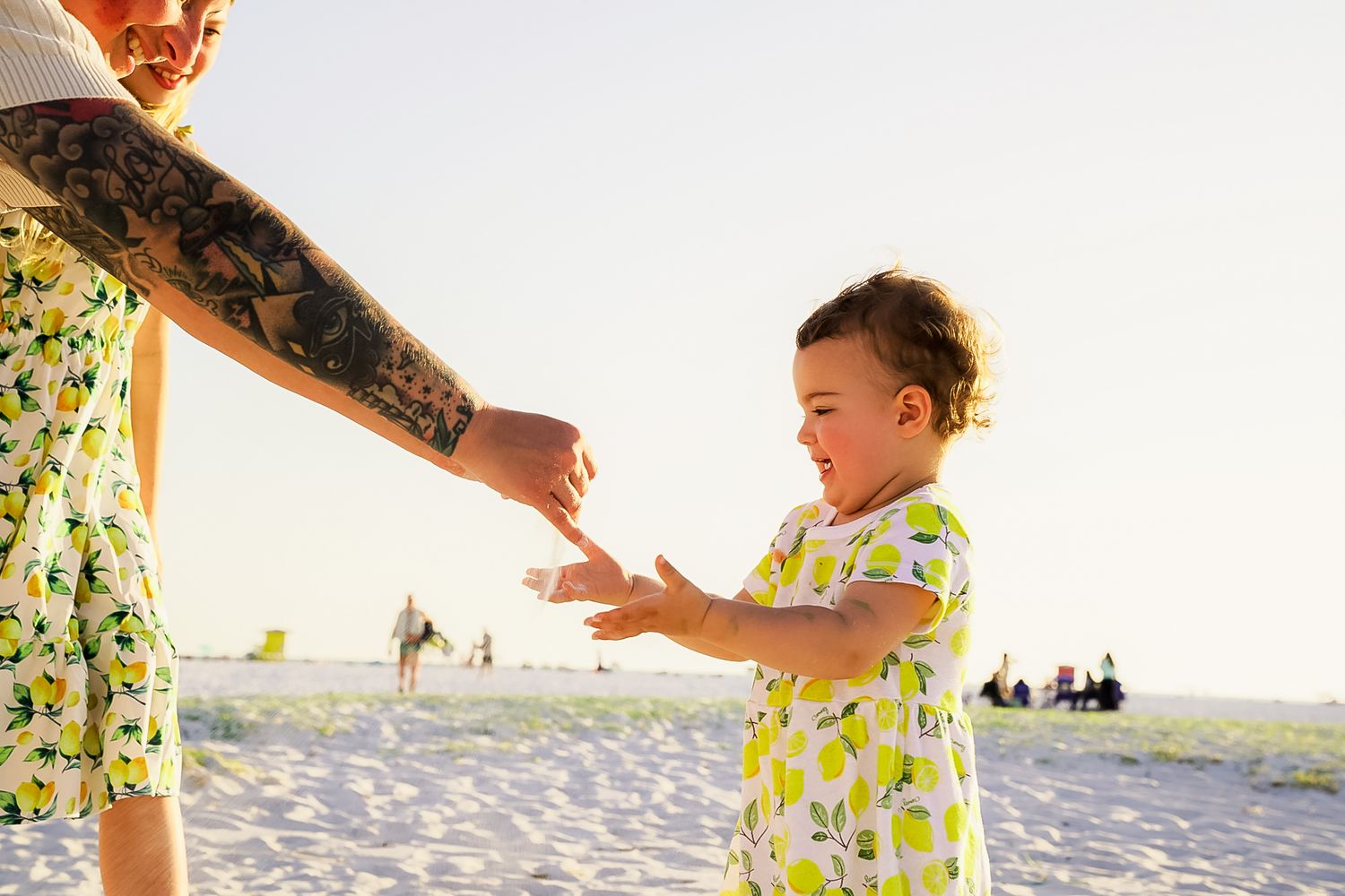 A photo of the little girl playing and smiling and laughing with sand behind her.