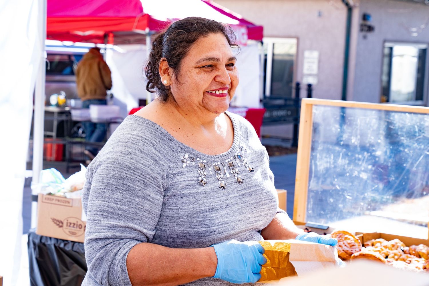 Smiling woman holding freshly baked bread at the farmers market, enjoying the local artisan food scene.