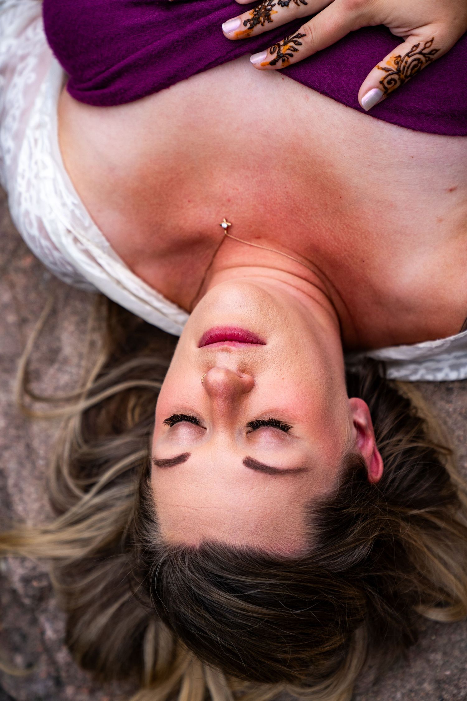 Portrait of someone lying down with eyes closed against purple fabric background.