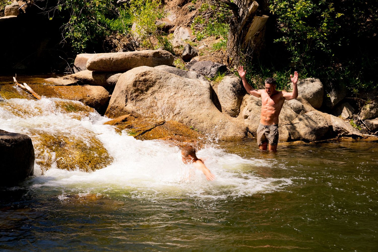 People swimming and playing in a natural rocky river waterfall outdoors.